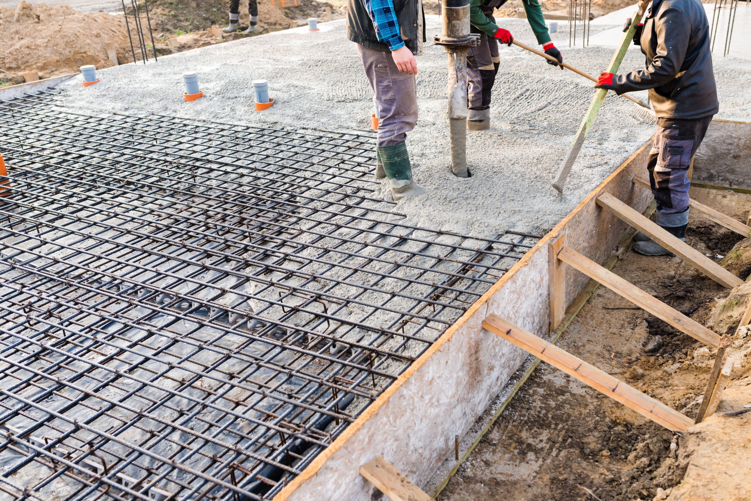 Construction workers pour concrete over a grid of steel rebar to create a building foundation after thorough site preparation. Wooden forms and pipes are visible as workers use tools to spread the concrete evenly. Bushcore Excavation Drainage Site Prep Grading Middle Tennessee Dickson Nashville